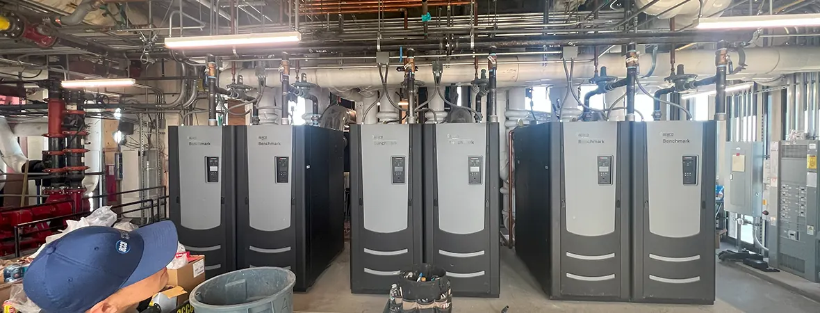 The bank of six AERCO BMK 5.0 condensing boilers in the penthouse mechanical room, re-grouped into two banks of three on common flues.